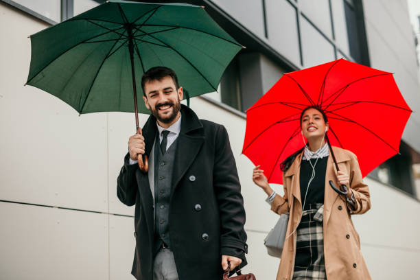 Loving married couple both business dressed meet after work in the city business center, both having umbrellas during a cloudy day.
