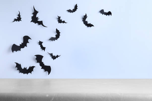 istock Empty grey table near white wall decorated with paper bats, space for text. Halloween celebration 1365534804