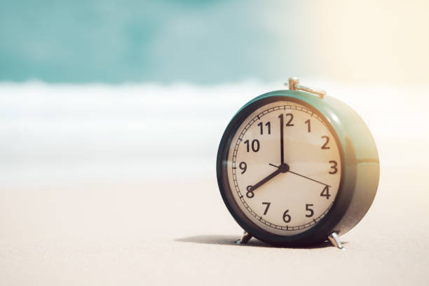 istock Clock on sand beach in morning suns light with smooth wave background. 1365536058
