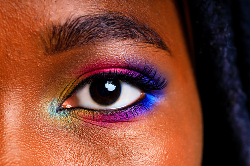 Female with rainbow make-up and long eyelashes in blue studio baclground.