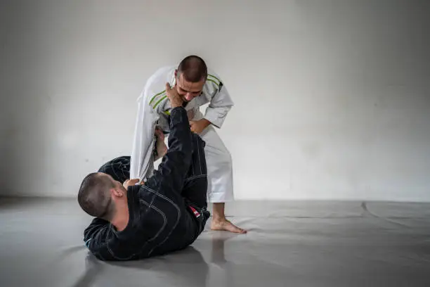 Two brazilian jiu jitsu bjj figters martial arts training male athlete practice technique or sparing at gym on tatami mat wearing black and white kimono gi uniform