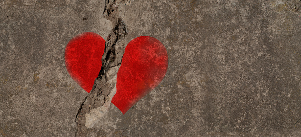 Red heart painted on a concrete wall and cracked in two. Copy space for additional content.