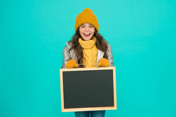 istock Fresh information. Schedule and working hours. Open hours. Winter entertainment and activities. Happy hours. Promotion concept. Smiling girl wear winter outfit show blank chalkboard copy space 1365539108