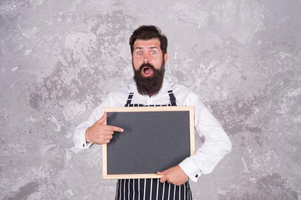 istock mature guy with beard and moustache is professional chef demonstrate cooking menu in cafe on empty chalkboard, dining services 1365539668
