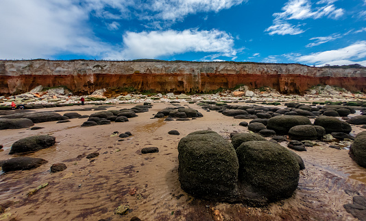 Wide angle direct face-on view of Old Hunstanton beach with rocks and orange striped cliffs and blue sky with clouds in upper third