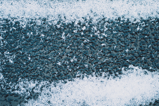 Close-up of a black bench covered with snow with a thin layer of ice