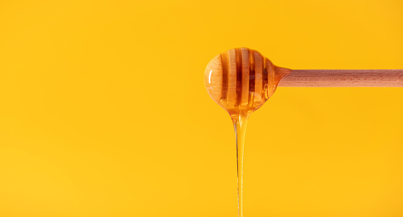 honey flowing from a wooden spoon on a yellow background with space for text