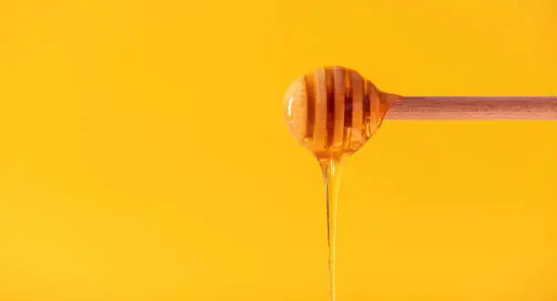 honey flowing from a wooden spoon on a yellow background with space for text
