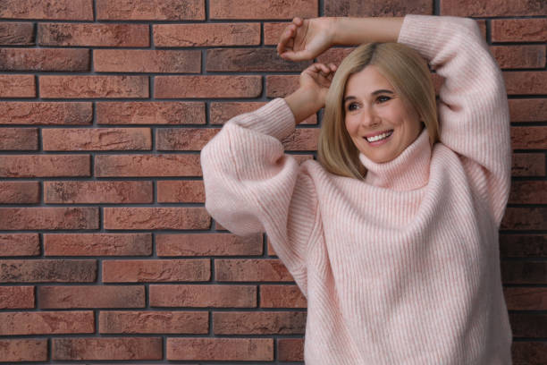 счастливая женщина в стильном свитере возле кирпичной стены. место для текста - brick red wool heat стоковые фото и изображения