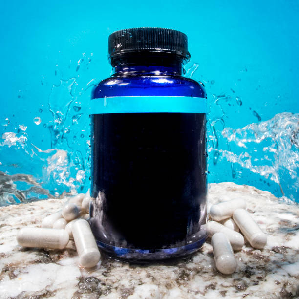 Medicine supplement pill bottle blank label on rock with blue background and water splashes Medicine supplement pill bottle blank label on rock with blue background and water splashes vitamin photos stock pictures, royalty-free photos & images