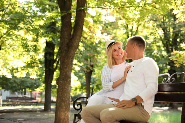 feliz pareja sentada en el banco en el parque de verano - pareja de mediana edad fotografías e imágenes de stock