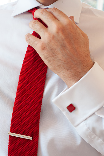 a man's hand adjusting his red tie