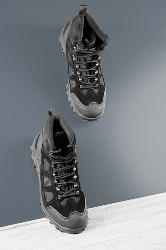 Close-up pair black textile work boots for safe winter with steel toe walking down inclined smooth gray metal surface.Non-slip effect demonstrating concept.Comfort flexible safety work wear,roofer