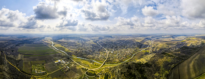 Aerial drone panorama view of a village located near a river and hills, fields, godrays, clouds in Moldova