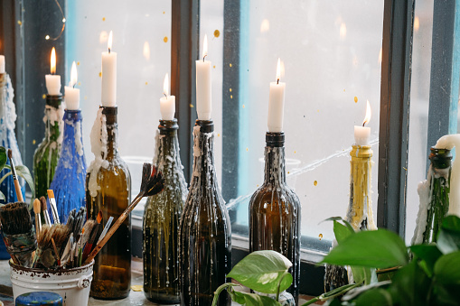 Candles in colorful bottles. melted wax, by the window. Natural light, creative atmosphere vintage look on windowsill