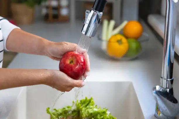 Photo of Woman washing a red apple in the sink in the kitchen