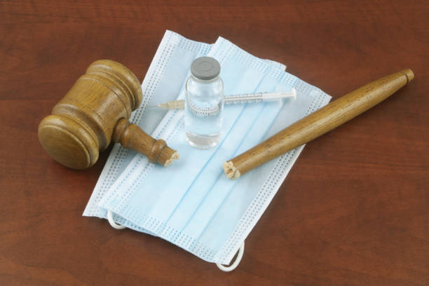 istock Broken judge gavel with vaccine bottle syringe and face masks on table. 1365566385