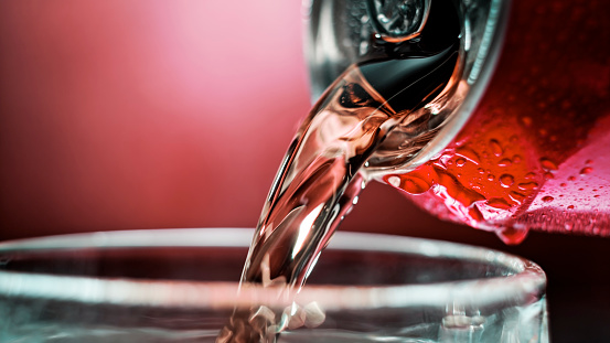 Close-up of cola pouring from tin can into glass against red background.