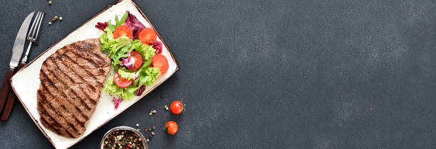 istock Grilled beef steak in a plate with salad and vegetables on a dark background. Dinner. 1365568854