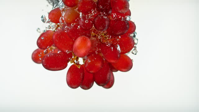SLO MO LD Cluster of red grapes falling into water against white background