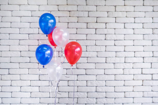 istock Close-up of multi-colored balloons against white brick wall background 1365569748