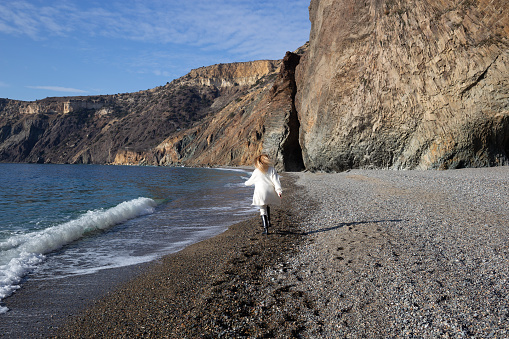 a young beautiful woman runs along a pebble beach against the backdrop of sea