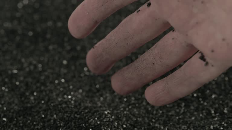 bare caucasian hand holding and pouring black activated carbon coconut charcoal powder of small fraction in slow motion