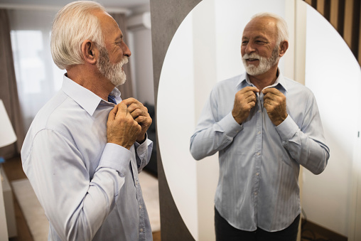 Portrait of a senior businessman looking at the mirror and getting dressed