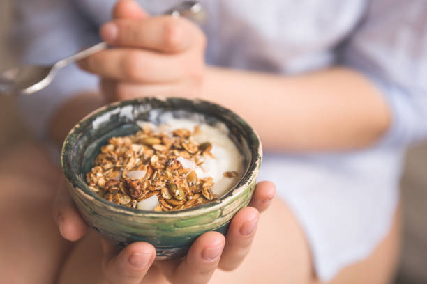 jeune femme avec bol de muesli. fille mangeant des céréales pour le petit-déjeuner avec des noix, des graines de citrouille, de l’avoine et du yogourt dans un bol. fille tenant du granola fait maison. collation saine ou petit-déjeuner le matin. - pumpkin seed food healthy eating photos et images de collection