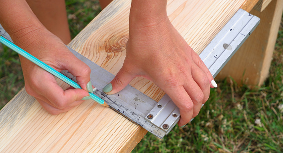 Woman carpenter makes pencil markings on a wooden board. DIY.