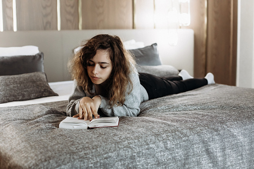 Teenager girl reading book on her bed