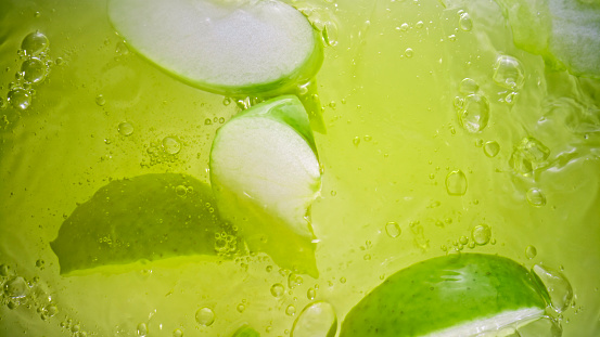 Close-up of apple wedges falling into apple juice.