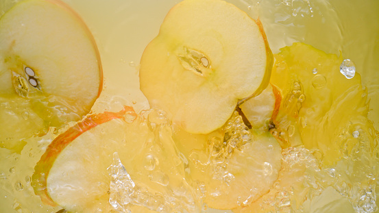 Close-up of apple slices falling into apple juice.