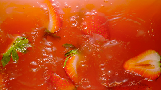 Close-up of cut fresh strawberries falling into red juice.