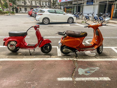 Valencia, Spain - October 9, 2021: Two red motor scooters in a row parked in dedicate space for them.  Their use became so extensive that the city government provides places to park them in the street