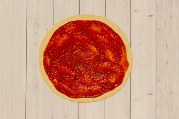 istock Spreading tomato sauce over a pizza dough on a wooden table. 1365589314