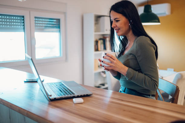 istock Middle aged woman drinking morning coffee and using a laptop at home 1365590339