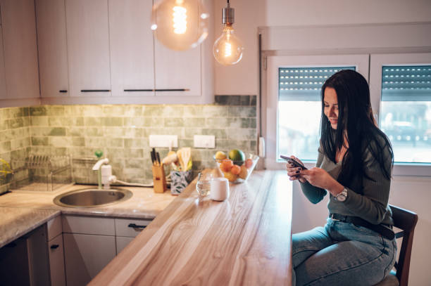 istock Middle aged woman using smartphone and drinking coffee in the kitchen at home 1365590354
