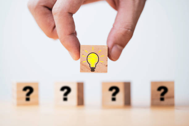 istock Hand putting lightbulb on wooden cube block in front of question mark for question and answer concept. 1365595387