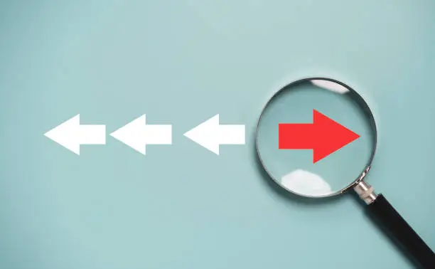 Photo of Red arrow inside of magnifier glass and different direction from white arrow for focus business disruption and technology transformation concept.