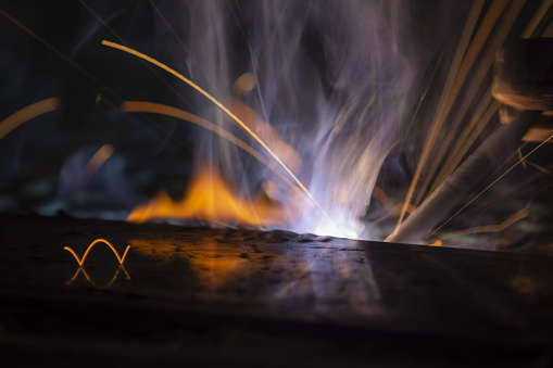 Close up of stick welding taking place, with bright lights, wisps of smoke, and flying sparks creating bright trails. Photo taken in Gainesville, Florida. Nikon D7200 with Nikon 200mm macro lens
