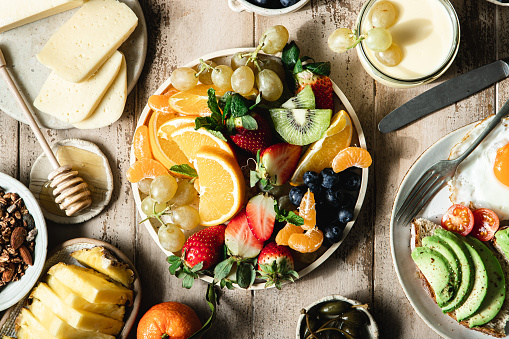 Close-up of variety of fruits in a plate with cheese slices, milk, honey. Full healthy breakfast served on table.