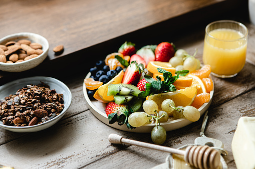 Mix fruits salad in a plate with chocolate granola, almonds and orange juice over wooden plate. Healthy breakfast served on kitchen table.