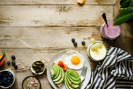 Top view of a healthy breakfast on wooden table with copy space. Avocado toast with fried egg served in a plate with milk and smoothie glasses.