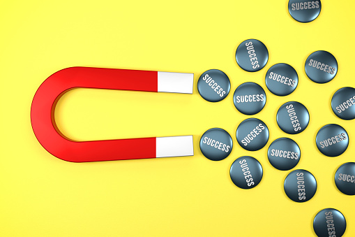 Metal Success Badges Gravitated Towards a Red Magnet on yellow background.