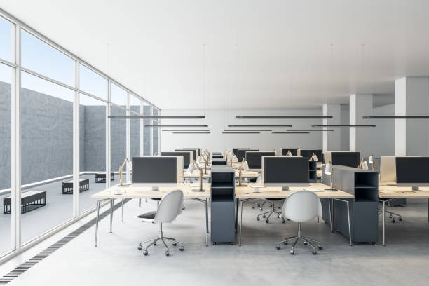 istock Modern coworking office interior with empty computer monitors on wooden desks, equipment, furniture and panoramic windows with daylight. 3D Rendering. 1365601377