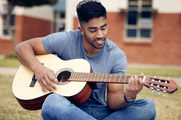 снимок молодого человека, играющего на гитаре на улице в колледже - 20s acoustic guitar adult art стоковые фото и изображения