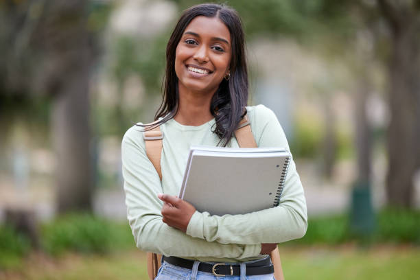 porträt einer jungen frau, die ihre schulbücher draußen am college trägt - universitätsstudent stock-fotos und bilder