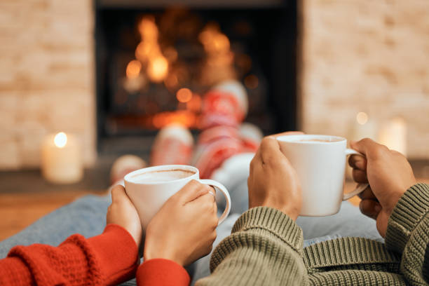 primer plano de una pareja tomando bebidas calientes mientras se relaja junto a una chimenea en casa - acogedor fotografías e imágenes de stock