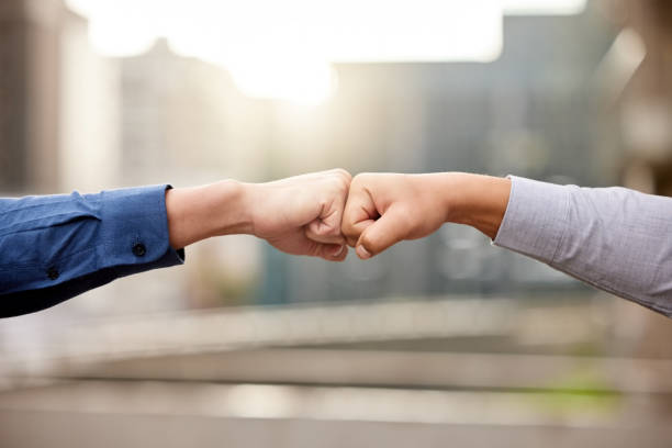 shot of two unrecognizable businesspeople fist bumping against a city background - zoom victory imagens e fotografias de stock